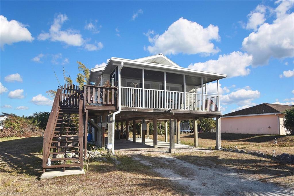 Back of property with a carport, a deck, dirt driveway, and a sunroom