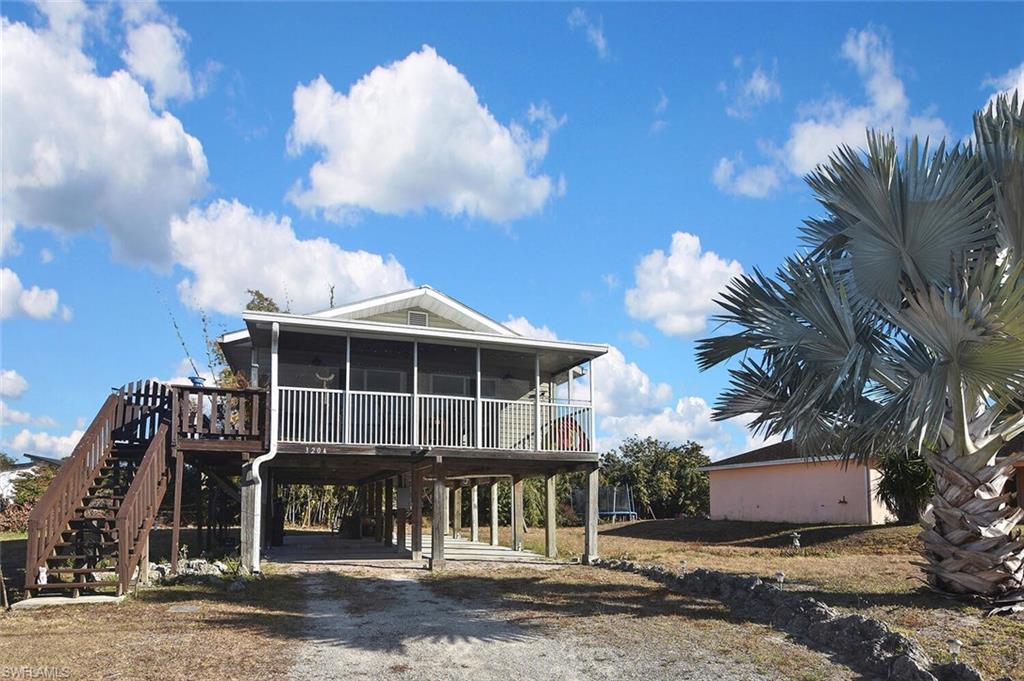 View of front of house with a sunroom, a wooden deck, a carport, and dirt driveway