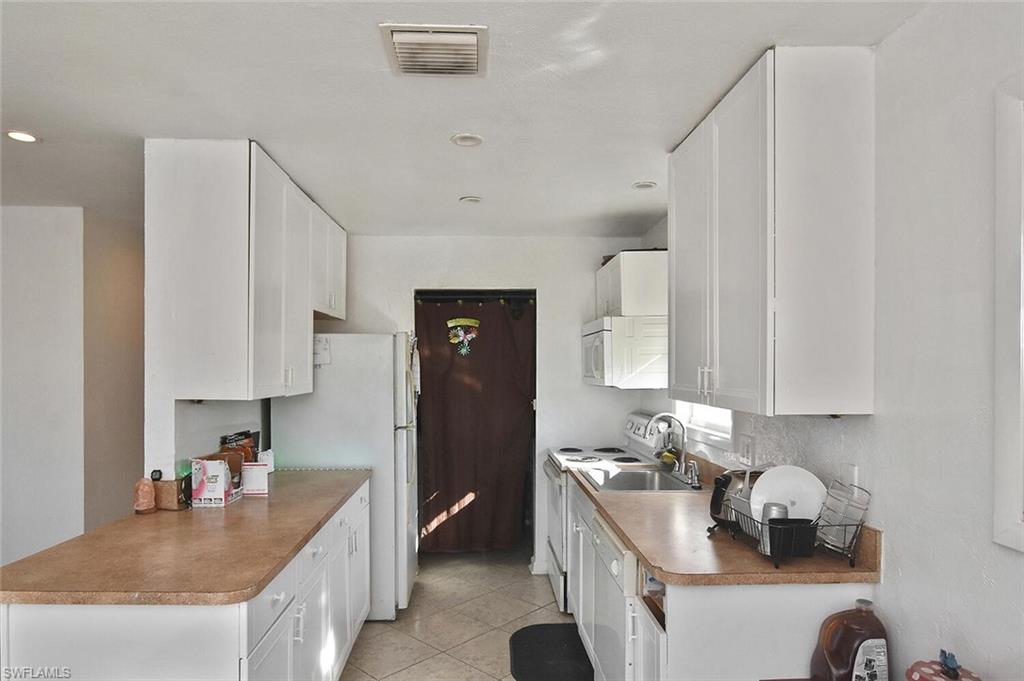 Kitchen featuring white cabinetry, white appliances, and light tile patterned flooring