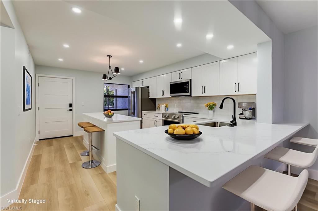 Kitchen featuring a breakfast bar area, a kitchen island, white cabinetry, light stone countertops, and light wood-type flooring