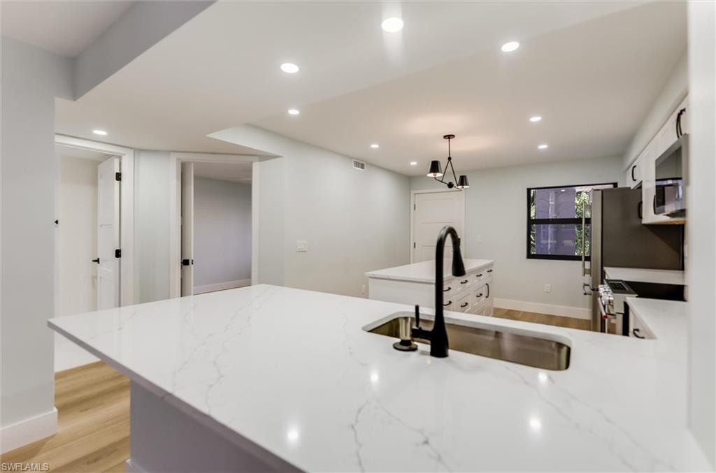 Kitchen with a peninsula, light wood-style floors, white cabinets, and light stone counters