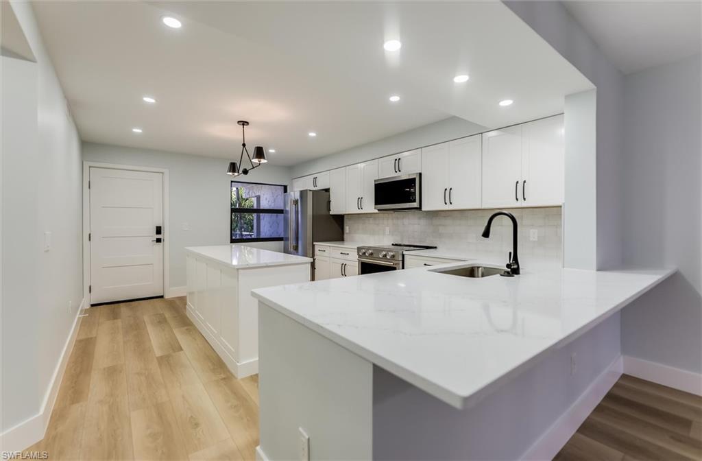 Kitchen featuring a center island, white cabinetry, light stone countertops, and stainless steel appliances