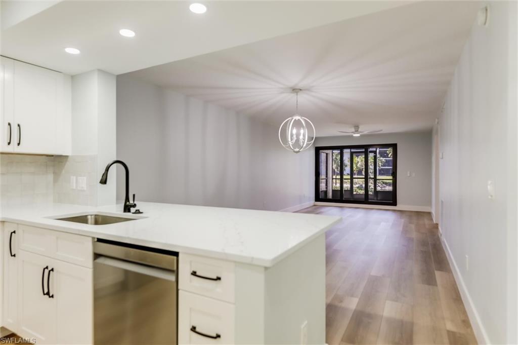 Kitchen with stainless steel dishwasher, open floor plan, light stone countertops, a peninsula, and light wood-type flooring