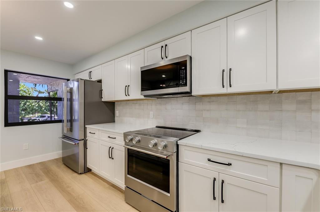 Kitchen with stainless steel appliances, white cabinets, light wood-type flooring, light stone countertops, and recessed lighting