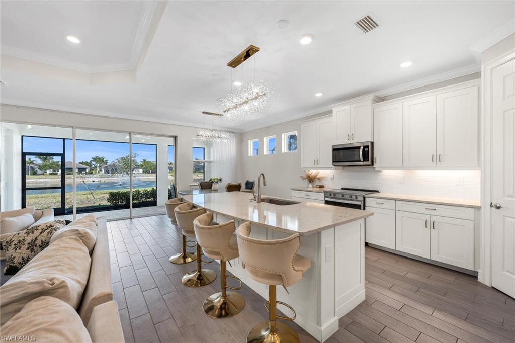 Kitchen featuring open floor plan, a kitchen island with sink, white cabinets, wood finish floors, and crown molding