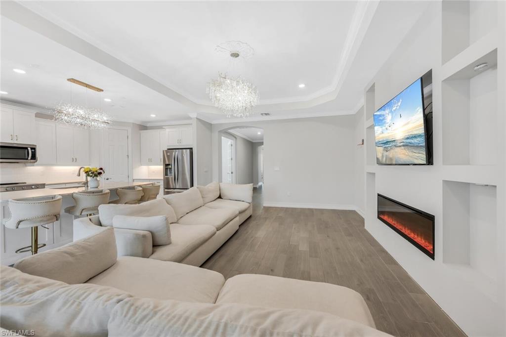 Living room with hanging lights, light wood-style flooring, arched walkways, a glass covered fireplace, and a tray ceiling