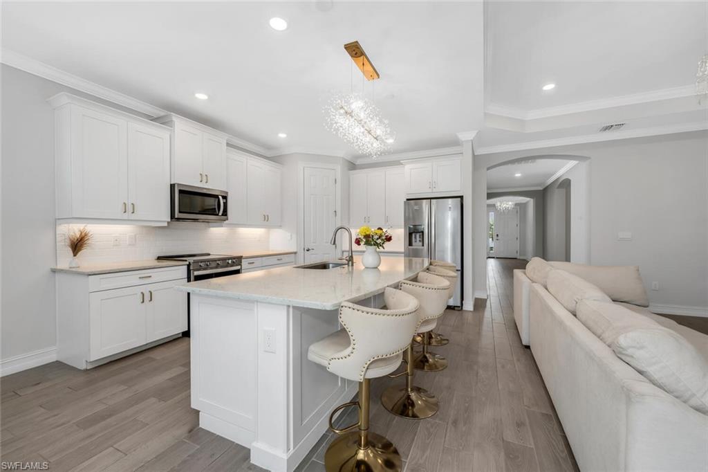 Kitchen featuring arched walkways, suspended lighting, backsplash, stainless steel appliances, and crown molding