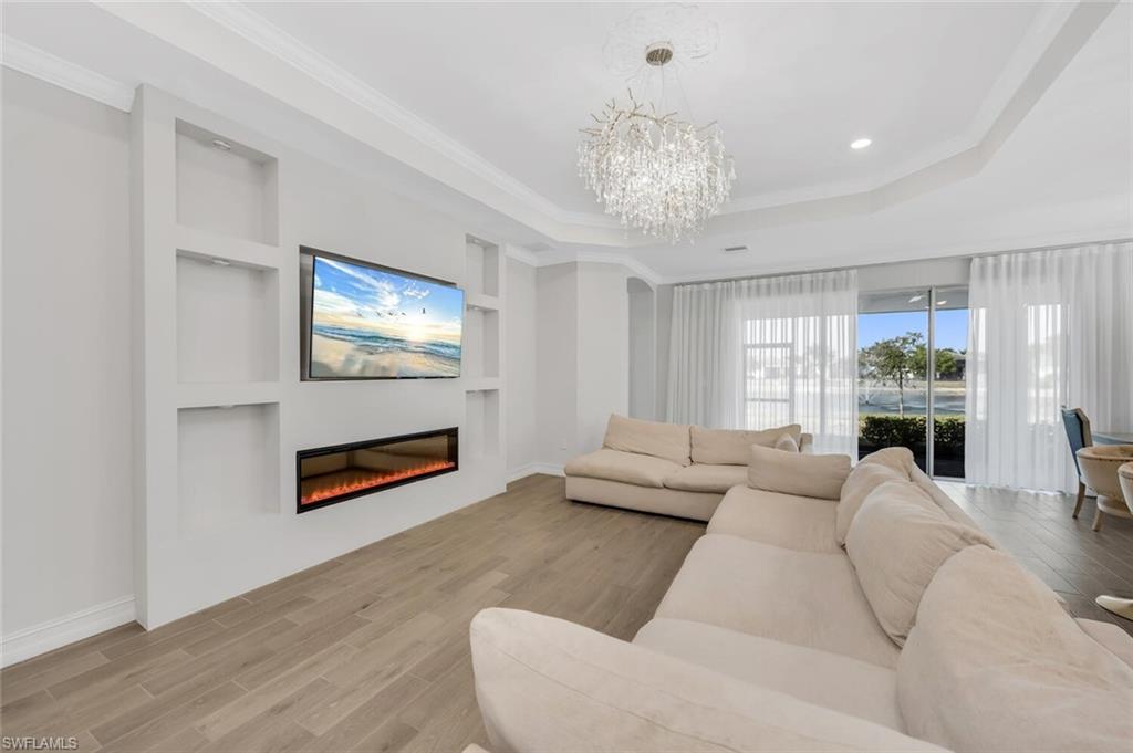 Living room with built in shelves, wood finished floors, hanging lights, crown molding, and a glass covered fireplace