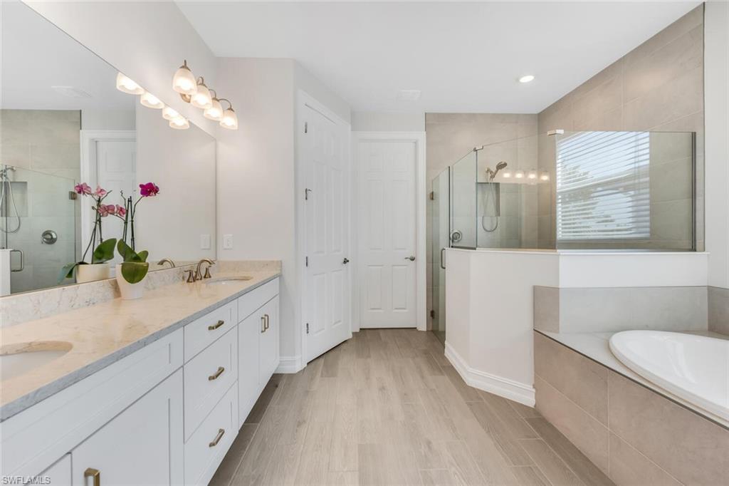 Bathroom featuring a stall shower, double vanity, light wood-style flooring, and a bath