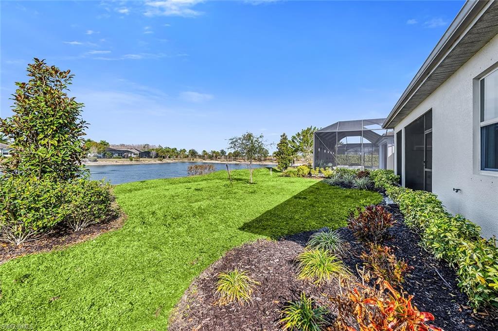 View of green lawn with a sunroom, glass enclosure, and a water view