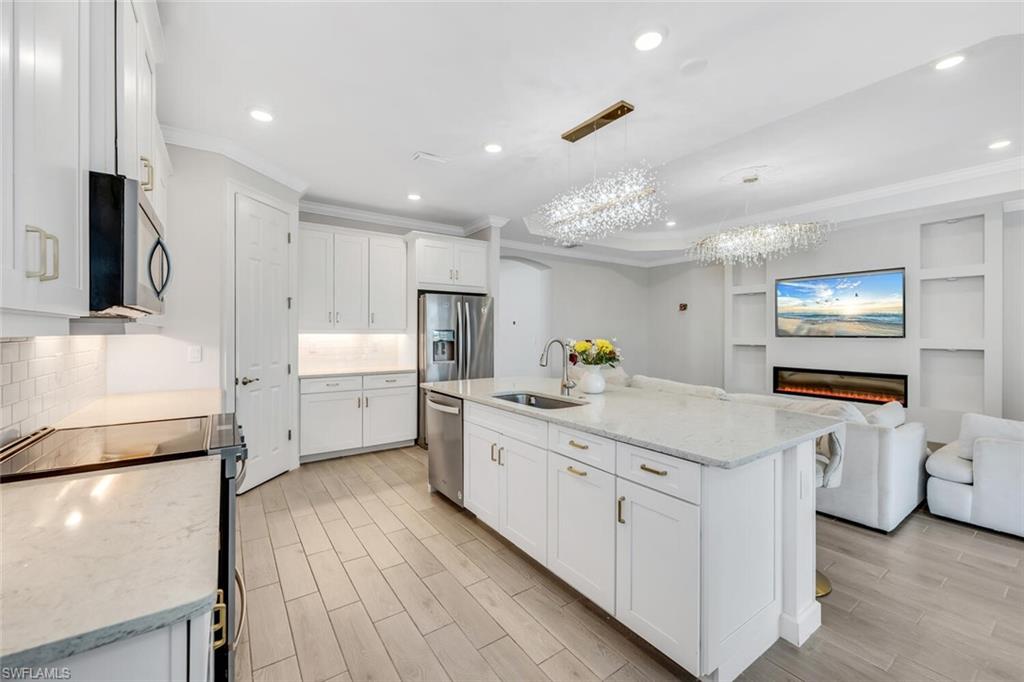 Kitchen with light stone countertops, stainless steel appliances, wood tiled floors, open floor plan, and white cabinetry