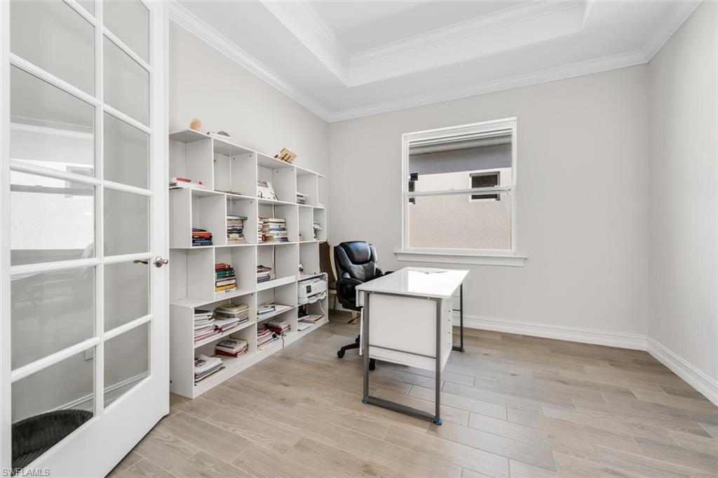 Home office with light wood-style flooring, a raised ceiling, and crown molding