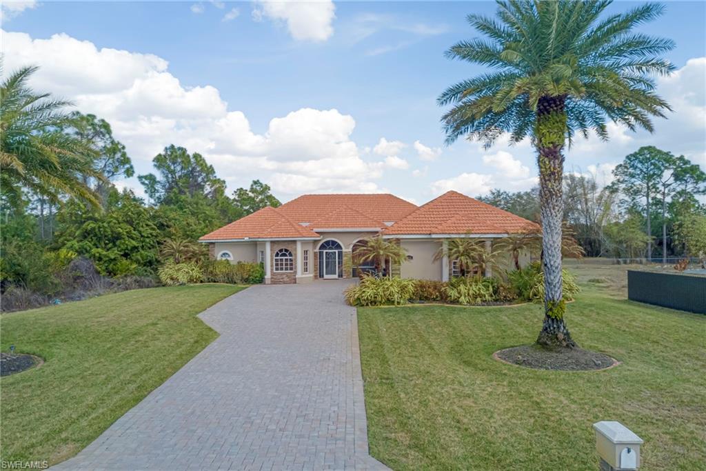Mediterranean / spanish-style house with a tile roof, stucco siding, decorative driveway, a front yard, and stone siding