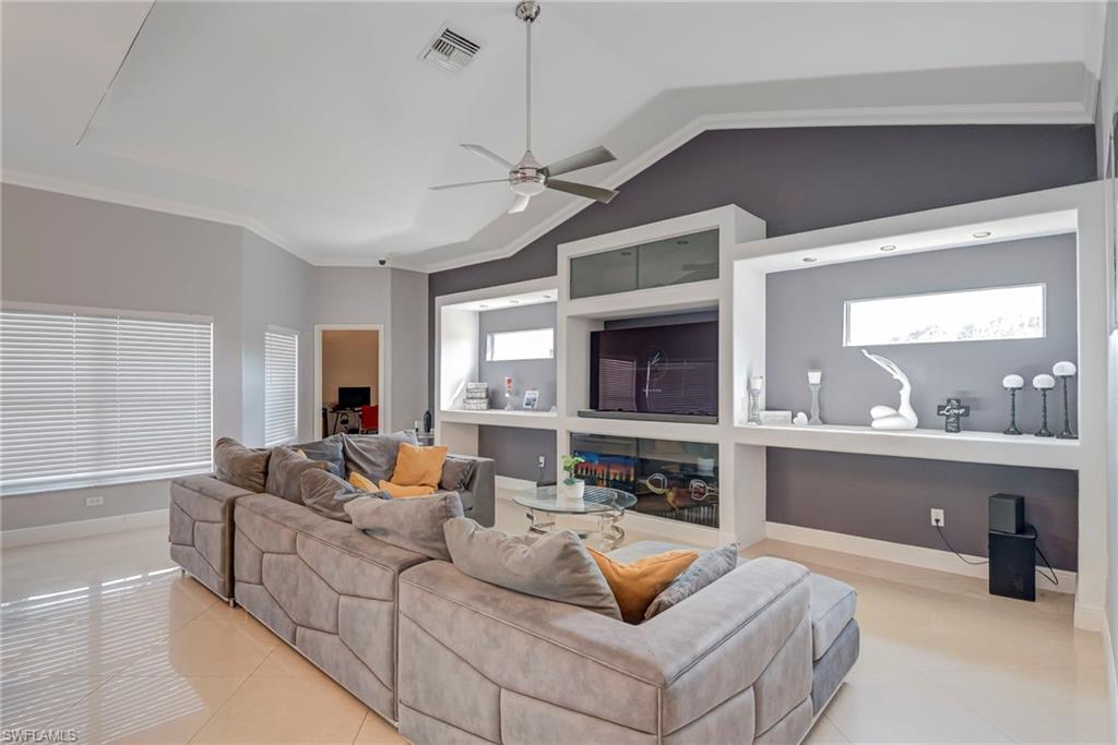 Living area with a ceiling fan, light tile patterned floors, crown molding, and a glass covered fireplace