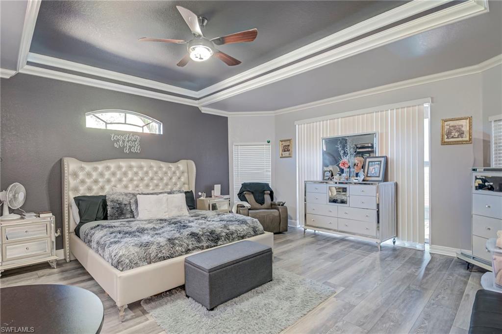 Bedroom with ornamental molding, wood finished floors, a tray ceiling, and a ceiling fan