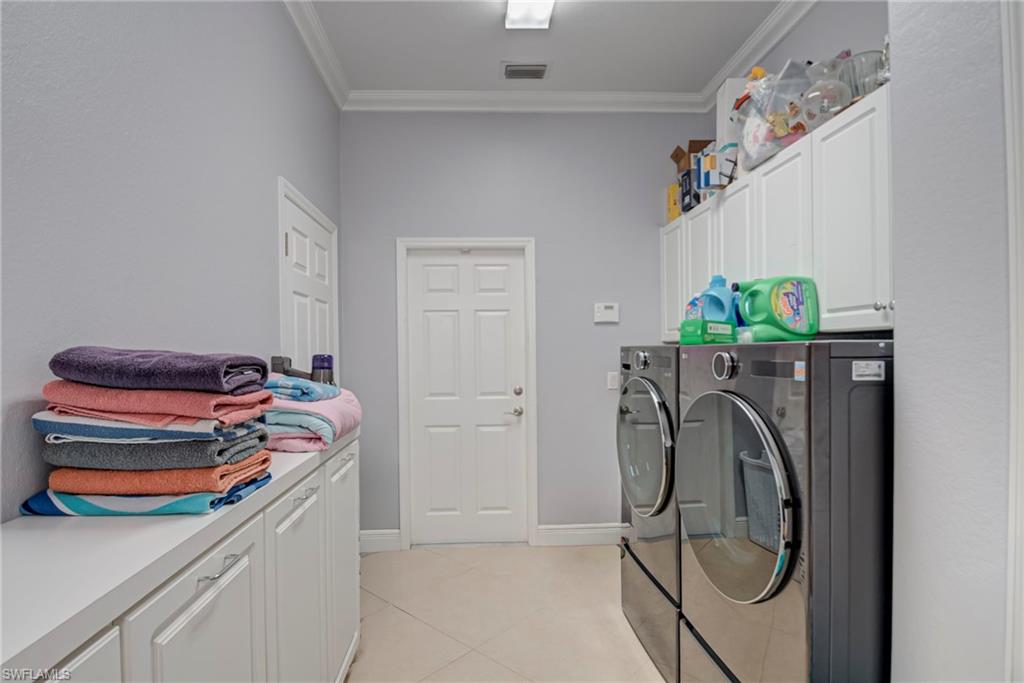 Laundry area with cabinet space, ornamental molding, washing machine and dryer, and light tile patterned floors