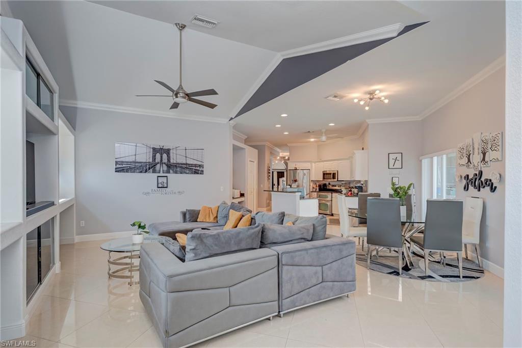 Living area featuring a ceiling fan, crown molding, light tile patterned floors, and a high ceiling