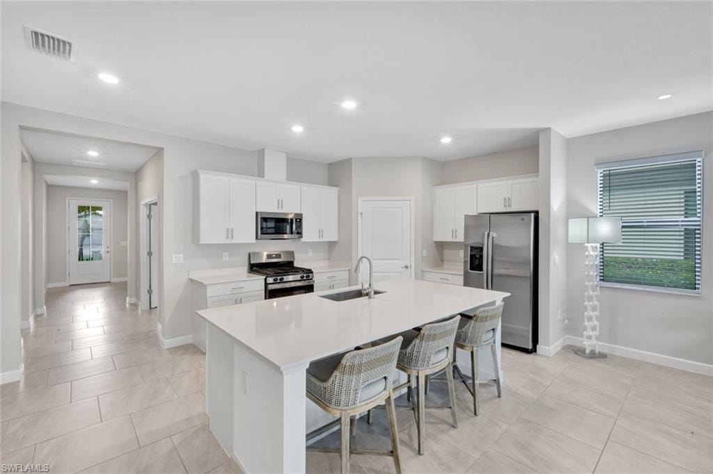 Kitchen with white cabinets, stainless steel appliances, a breakfast bar area, a kitchen island with sink, and recessed lighting