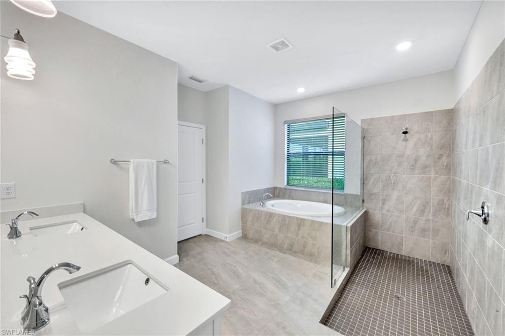 Full bath with double vanity, a walk in shower, a garden tub, light tile patterned flooring, and recessed lighting