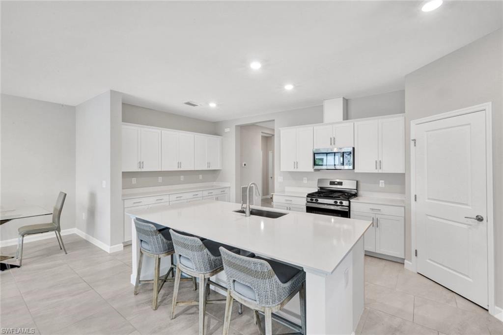 Kitchen featuring stainless steel appliances, a kitchen breakfast bar, white cabinetry, an island with sink, and light stone countertops