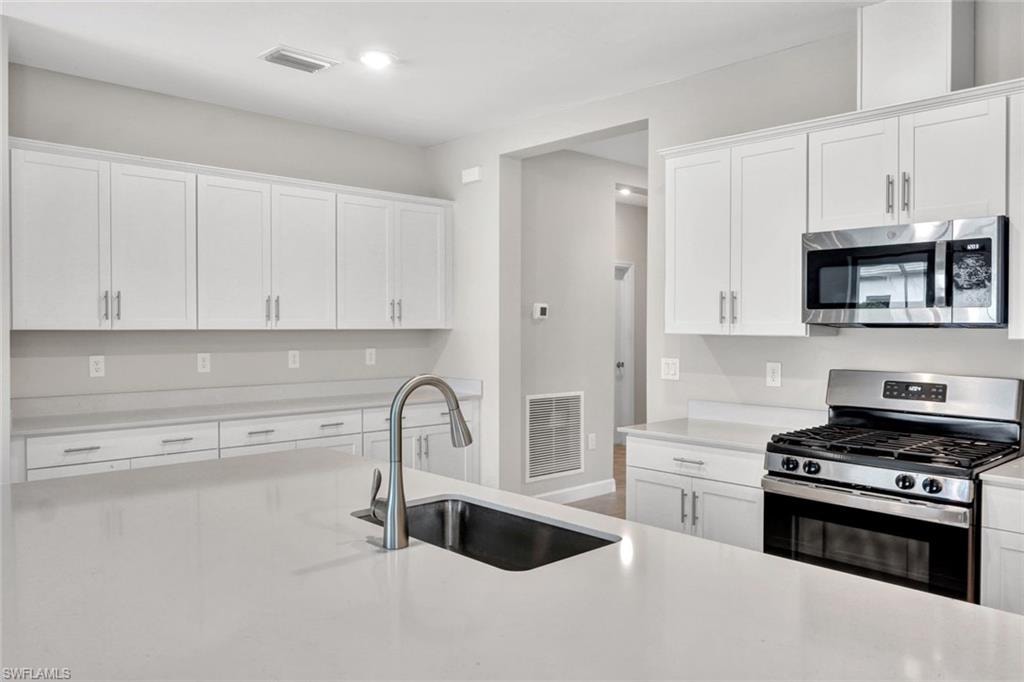 Kitchen featuring stainless steel appliances, white cabinets, and light stone countertops