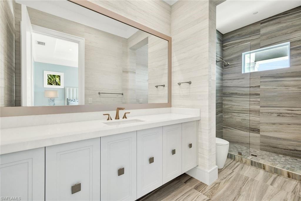 Bathroom featuring a walk in shower, vanity, and tile walls