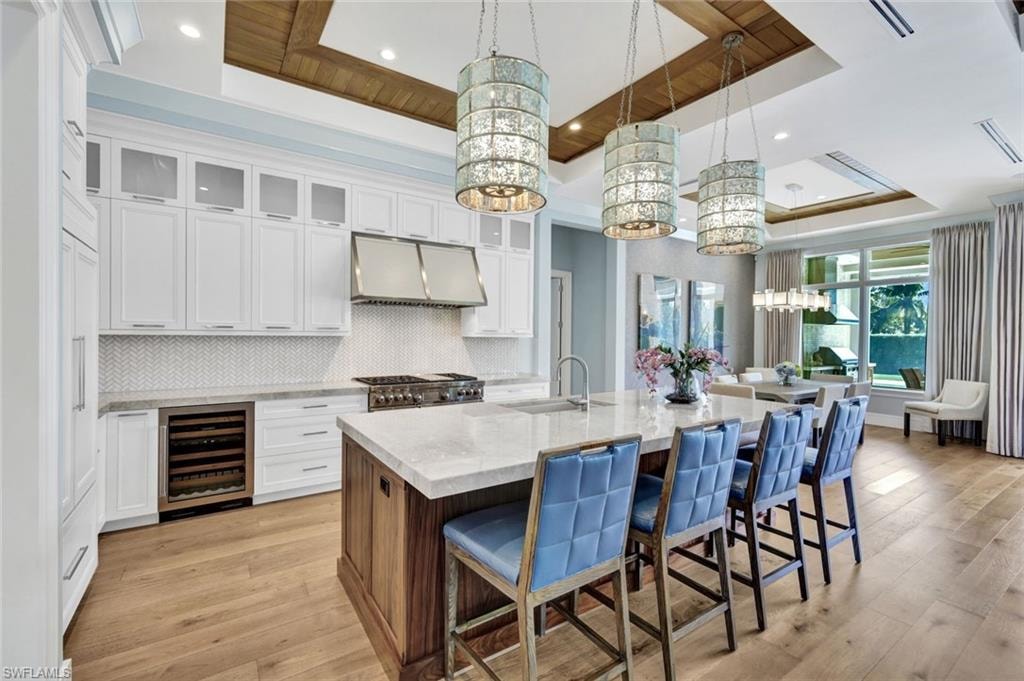 Two tone kitchen with a tray ceiling, a kitchen bar, dual tone cabinets, glass insert cabinets, and light stone countertops