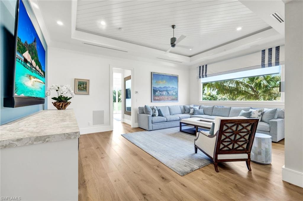 Living area with light wood-style floors, a ceiling fan, a wood tray ceiling, and recessed lighting