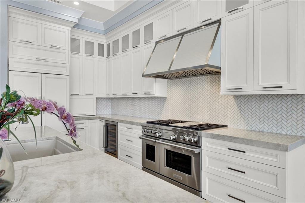 Kitchen with glass fronted cabinets, double oven range, light stone counters, wine cooler, and white cabinets