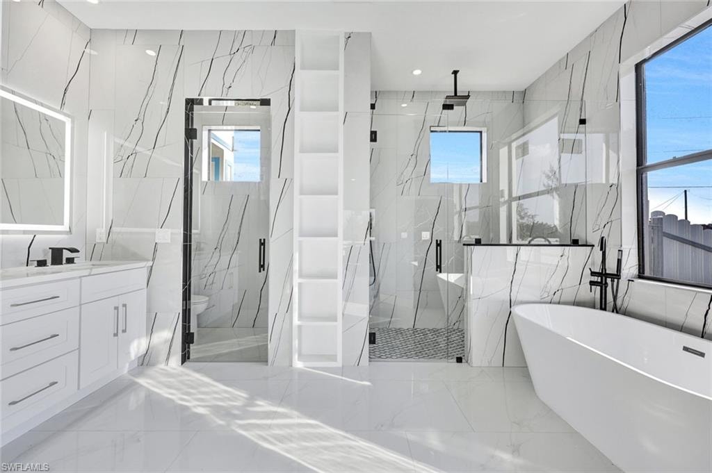 Full bath featuring a freestanding bath, light marble finish floors, a marble finish shower, plenty of natural light, and recessed lighting