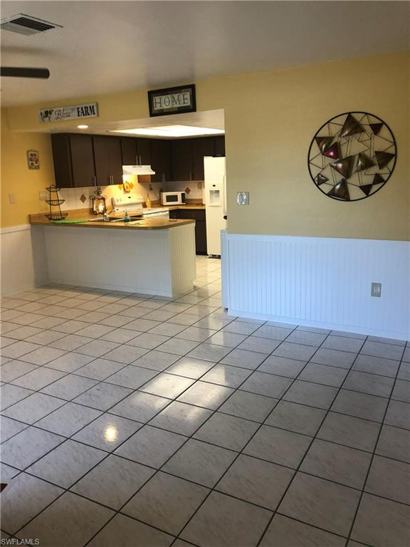 Kitchen featuring wainscoting, a peninsula, white appliances, light tile patterned flooring, and a ceiling fan