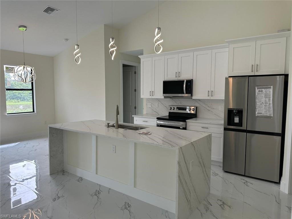 Kitchen featuring stainless steel appliances, light stone counters, white cabinets, backsplash, and vaulted ceiling