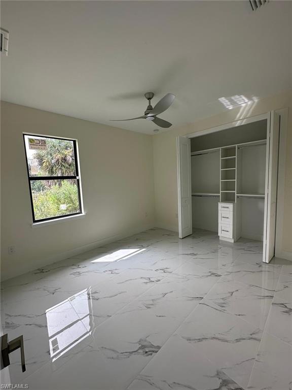 Unfurnished bedroom with a closet, light marble finish flooring, and a ceiling fan
