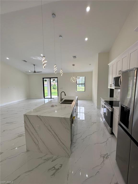 Kitchen with pendant lighting, stainless steel appliances, open floor plan, light stone countertops, and an island with sink