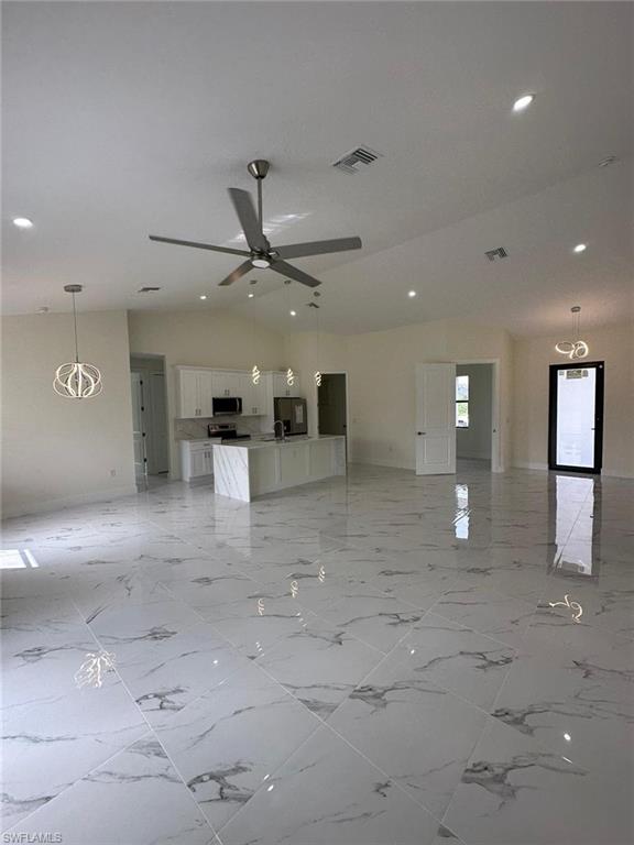 Unfurnished living room with vaulted ceiling, a ceiling fan, and suspended lighting