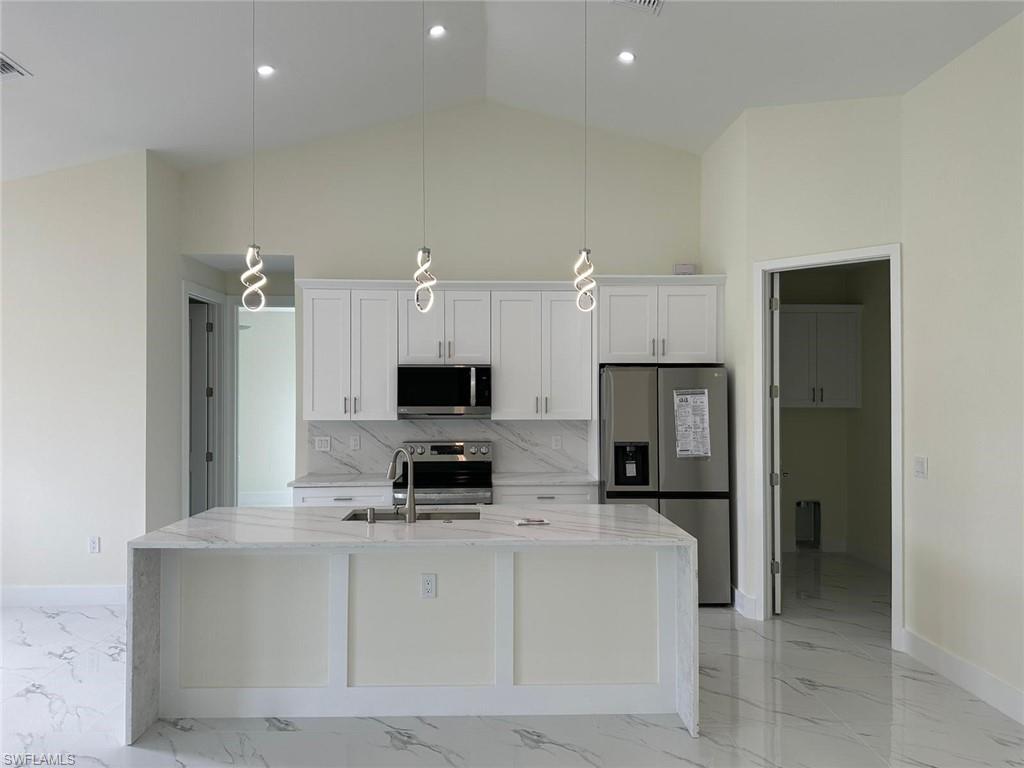 Kitchen featuring light stone countertops, stainless steel appliances, white cabinets, hanging light fixtures, and a center island with sink