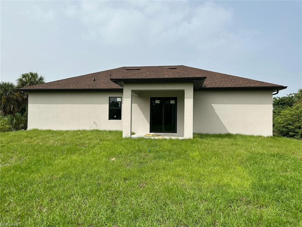 Rear view of house with a yard, stucco siding, a patio area, and a shingled roof