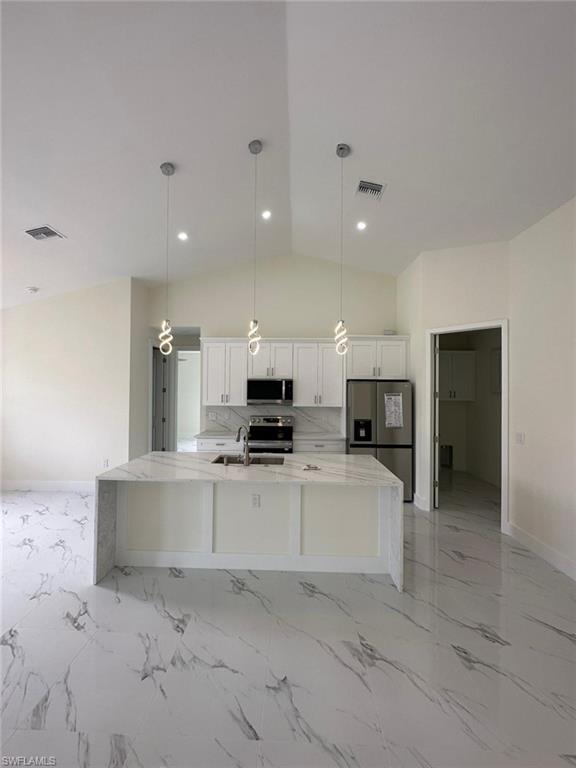 Kitchen featuring light stone counters, hanging light fixtures, stainless steel appliances, white cabinetry, and a kitchen island with sink