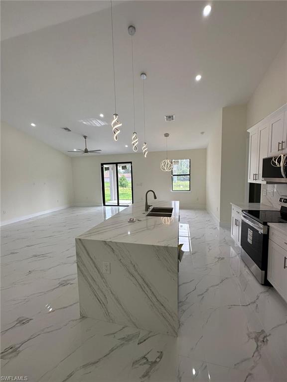 Kitchen with decorative light fixtures, stainless steel appliances, open floor plan, and white cabinets