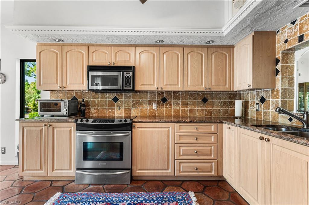 Spacious kitchen features granite counters, tile backsplash, custom cabinets, stainless steel appliances, and a built-in desk area