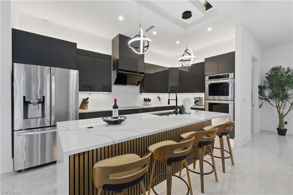 Kitchen with stainless steel appliances, light stone countertops, a breakfast bar area, and dark cabinets