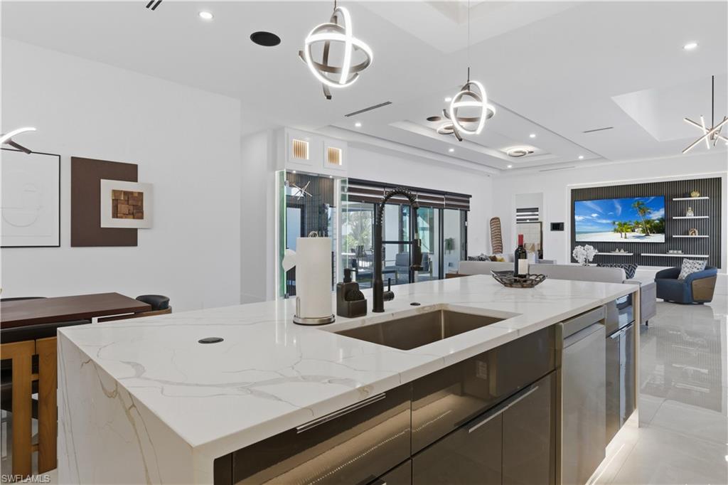 Kitchen featuring open floor plan, light stone countertops, a kitchen island with sink, modern cabinets, and hanging light fixtures