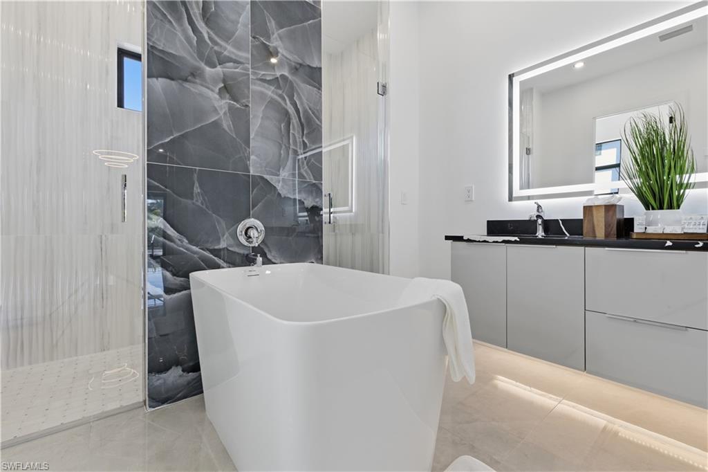 Full bathroom featuring vanity, a soaking tub, and a marble finish shower