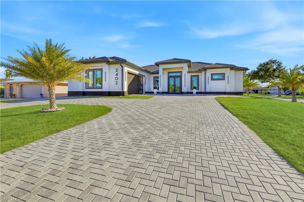 Prairie-style house featuring a front yard, decorative driveway, an attached garage, and stucco siding