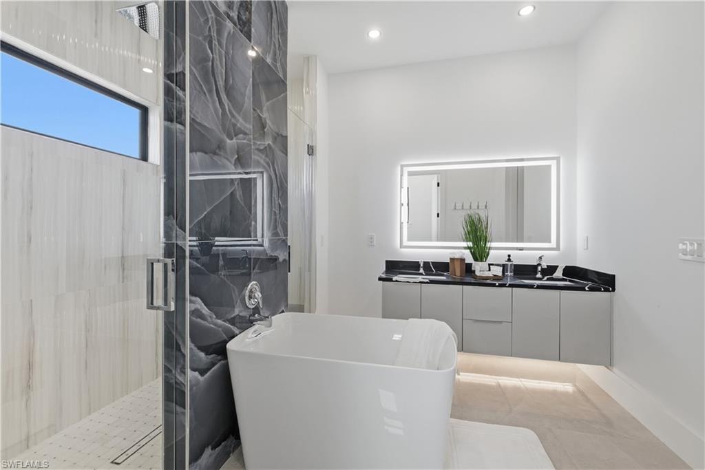Bathroom featuring double vanity, a marble finish shower, a soaking tub, and recessed lighting