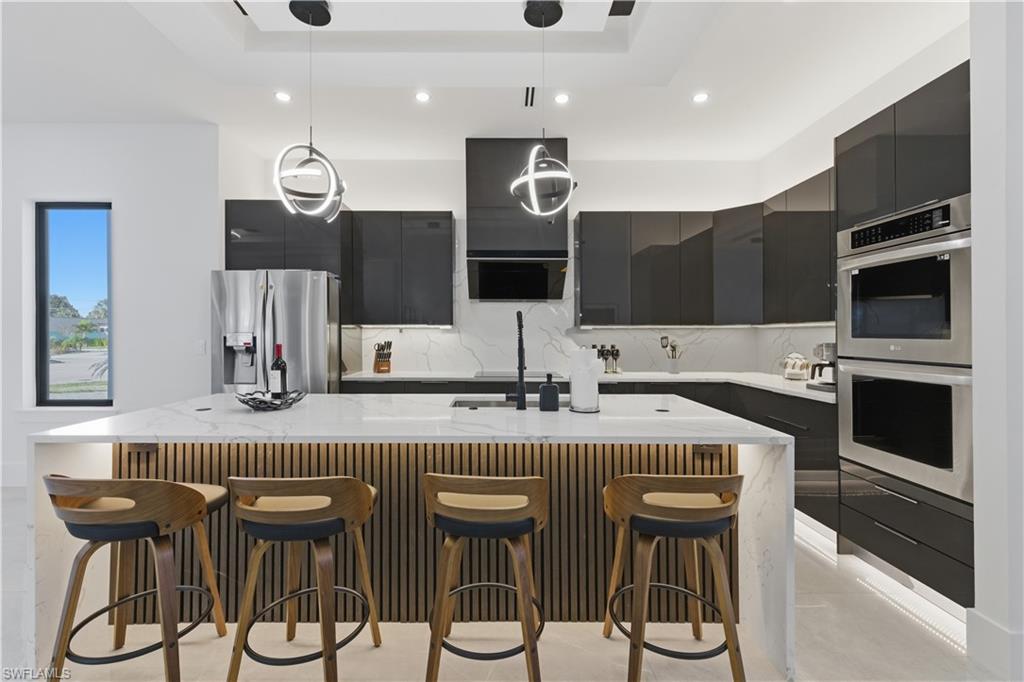 Kitchen with modern cabinets, a kitchen breakfast bar, light stone counters, an island with sink, and pendant lighting