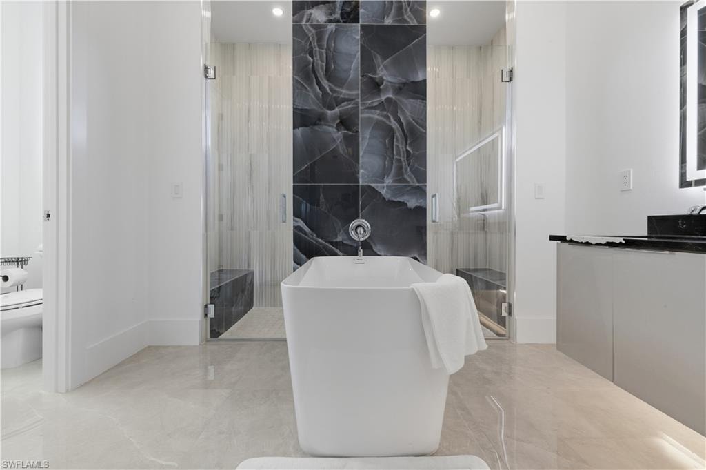 Full bathroom featuring a marble finish shower, a soaking tub, tile walls, light marble finish floors, and vanity