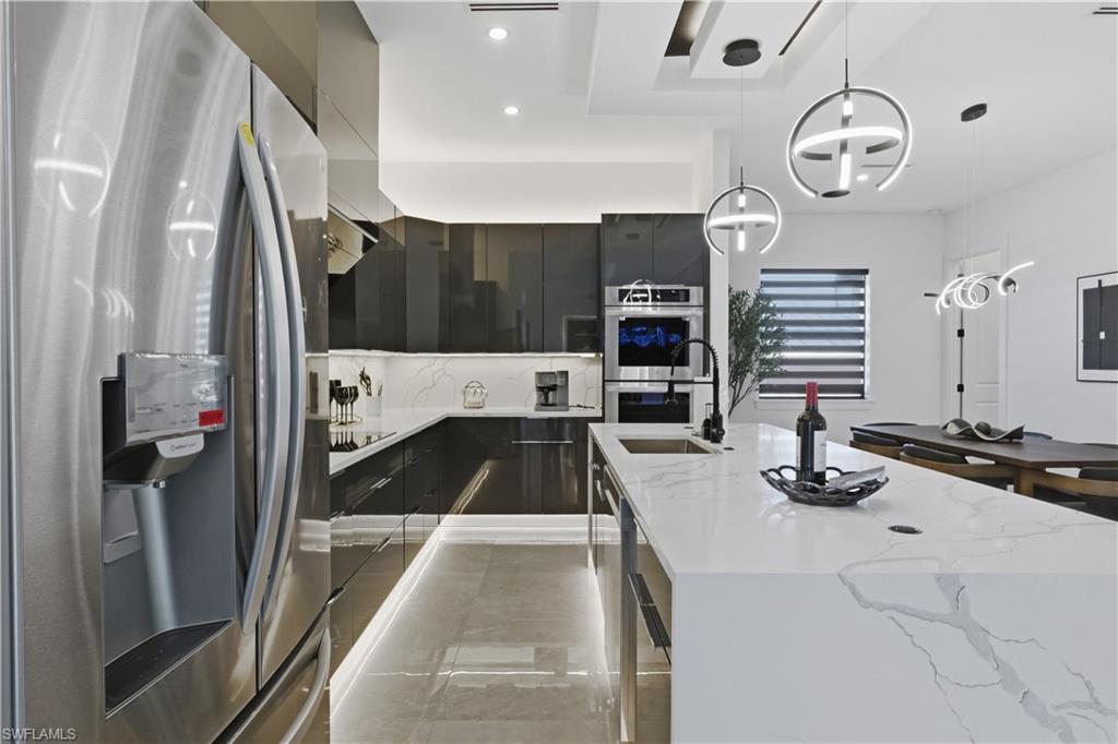 Kitchen featuring decorative light fixtures, stainless steel appliances, modern cabinets, light stone countertops, and dark cabinets