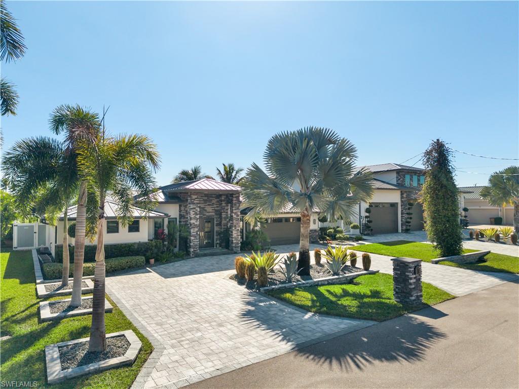View of property hidden behind natural elements featuring curved driveway, a front yard, stone siding, stucco siding, and a garage