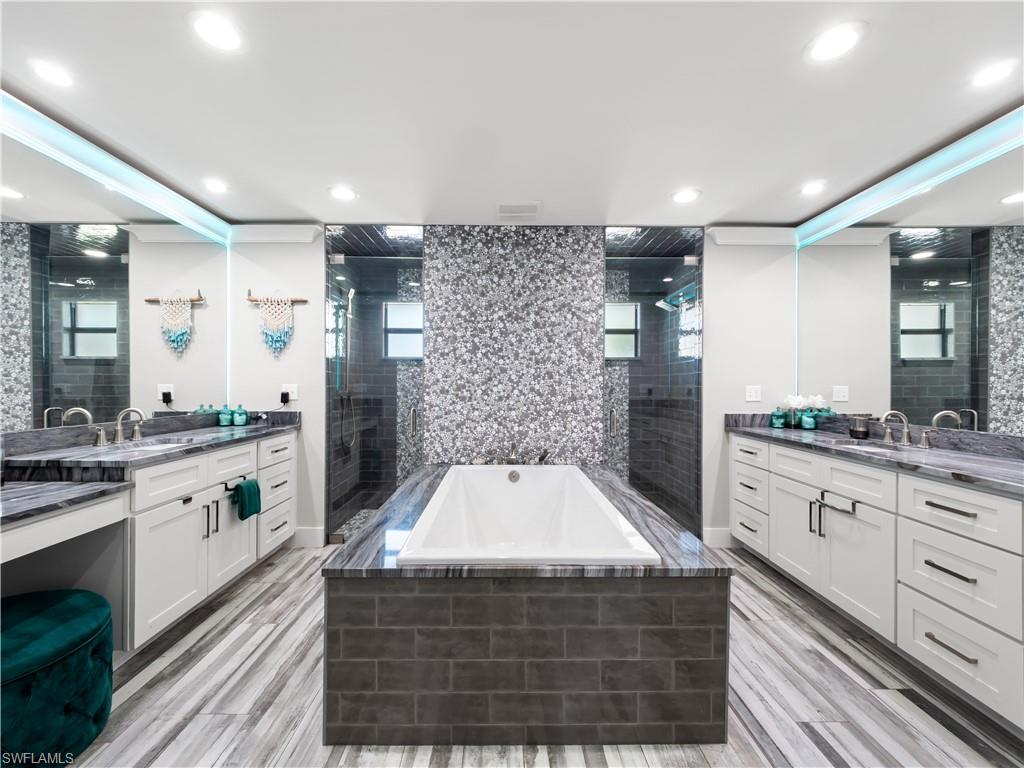 Bathroom with two vanities, a bath, tiled shower, and light wood finished floors